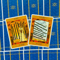 Tarot kortos devynetas ir aštuonetukas (lazdelės), oranžiniai priekiniai variantai, dvi kortos pasvirusios ant mėlyno raštuoto užnugario