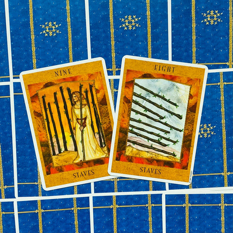 Tarot kortos devynetas ir aštuonetukas (lazdelės), oranžiniai priekiniai variantai, dvi kortos pasvirusios ant mėlyno raštuoto užnugario