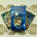 Fantastical Creatures Tarot kortų rinkinys su mėlynu dėklu ir trimis iliustruotomis kortomis, išskleistomis ant aukso ornamentų fono
