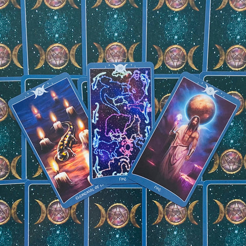 Tarot kortos su mėlynu apvadu — trys atvertos kortos: salamandra prie žvakių, žvaigždžių konstelacijos ir burtininkas