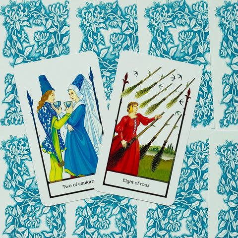 tarot kortos Rider–Waite stiliaus dviejų kortų išklotinė: Two of Cauldrons ir Eight of Rods ant mėlyno ornamentuoto fono