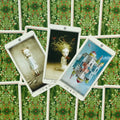 Tarot kortos trijų kortų išklotinė ant žaliu lapų rašto fono, centre mergaitė su išsišakojusiais plaukais ir paukščiais, dešinė korta apversta