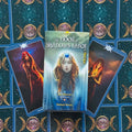 Prekės vaizdas: The Book of Shadows Tarot Volume 1 dėžutė priekyje, fanuotos mėlynos kortos su mėnulio simboliais ir dvi iliustruotos kortos šone