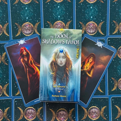 Prekės vaizdas: The Book of Shadows Tarot Volume 1 dėžutė priekyje, fanuotos mėlynos kortos su mėnulio simboliais ir dvi iliustruotos kortos šone