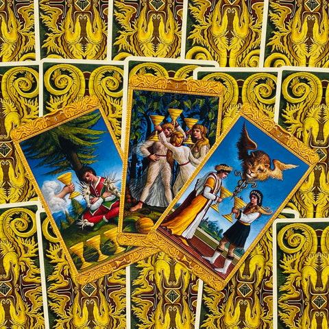 Tarot kortos — trys atvertos taurų rūšies kortos su auksiniu rėmu ant geltonos ornamentuotos nugarėlės, detalus priekis
