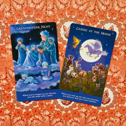 Oracle kortos dvi kortos (mėlynos ir violetinės) plokščiai ant oranžinio gėlių audinio, matomi skirtingi iliustracijų pavadinimai