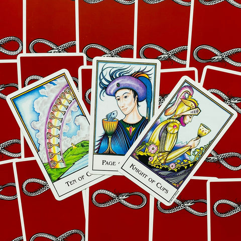 Tarot kortos su raudonomis nugarėlėmis, trys atverstos Taurių kortos (Ten of Cups, Page of Cups, Knight of Cups) išdėstytos fane