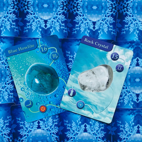 Orakulinės kortos ant mėlyno snaigių fono, dvi atverstos kortos išryškina Blue Howlite ir Rock Crystal variantus