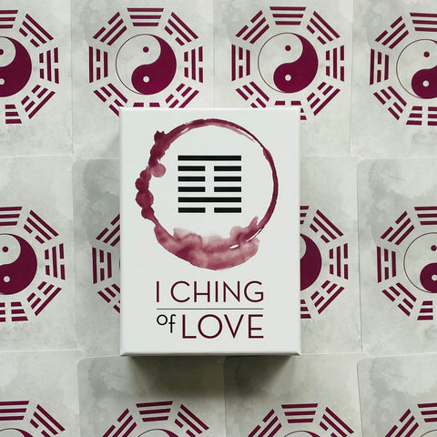 I Ching of Love kortų rinkinys baltame dėkle su purpuriniu simboliu ir vingiuotu žiedu, centre ant yin‑yang fono