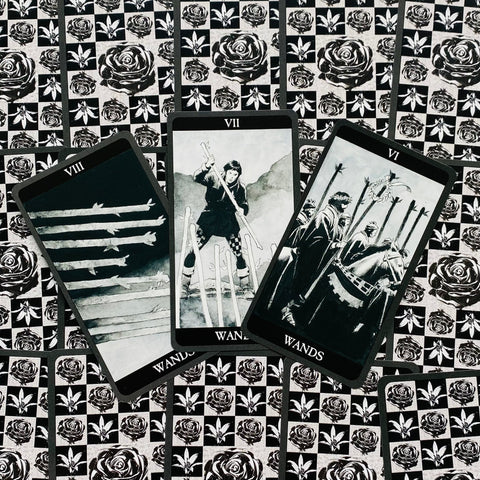 tarot kortos juodai baltos Rider‑Waite stiliaus, trijų lazdų išklotinė centre, rožių motyvai nugarėlėse
