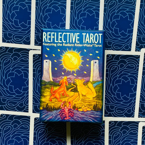 Tarot kortos Reflective Tarot, Radiant Rider‑Waite leidimas mėlyname dėkle, priekinis kampas prieš tamsiai mėlyną modeliuotą kortų nugarėlių foną