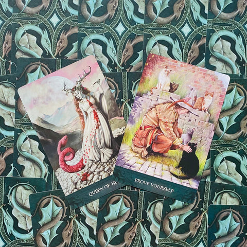 tarot kortos su dviem atverstomis kortomis Queen of Hearts ir Prove Yourself ant žalsvų drakonų nugarėlių, detalesni iliustruoti motyvai