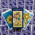 Universal Wirth Tarot dėžutė centre su klajūno iliustracija, fone violetinės kortų nugarėlės ir dvi Lazdų rūšies kortos šonuose