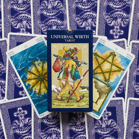 Universal Wirth Tarot dėžutė centre su klajūno iliustracija, fone violetinės kortų nugarėlės ir dvi Lazdų rūšies kortos šonuose
