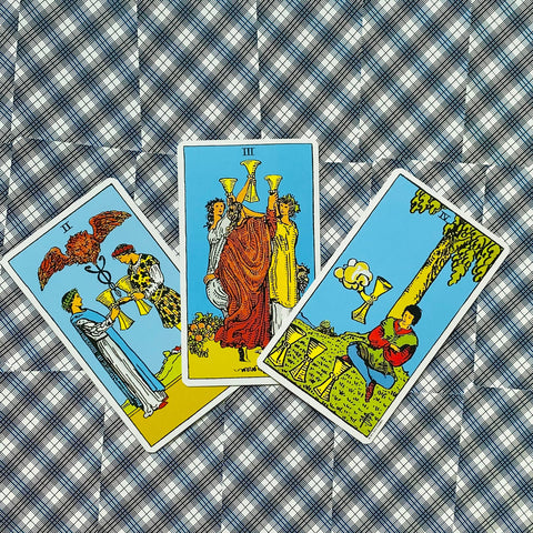 tarot kortos Rider–Waite taurės: trijų kortų išdėstymas iš viršaus ant mėlynos languotos drobės, parodyta kortų variacija