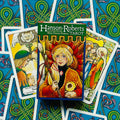 Hanson‑Roberts tarot kortų rinkinys, spalvota iliustruota dėžutė centre ir kelios išskleistos kortos mėlyname fone