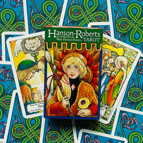 Hanson‑Roberts tarot kortų rinkinys, spalvota iliustruota dėžutė centre ir kelios išskleistos kortos mėlyname fone