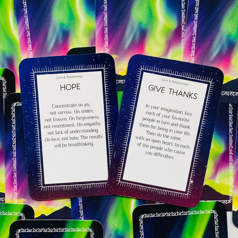 Orakulų kortos su ryškiu šiaurės pašvaistės fonu, dvi atvertos kortos Hope ir Give Thanks skirtos santykių įžvalgoms