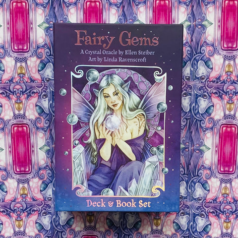 Orakulo kortų rinkinys Fairy Gems purpuriniame dėkle su fėjos iliustracija, kristalais ir rožinės–mėlynos raštuotos fono detalėmis