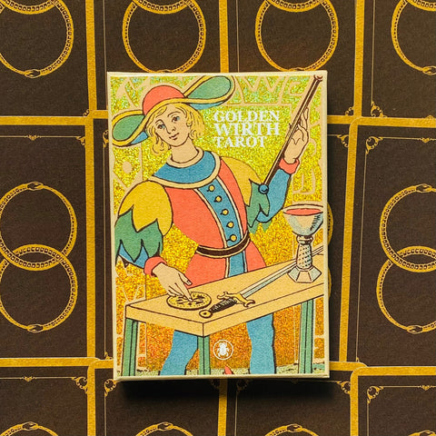 Tarot kortos Golden Wirth, blizganti auksinė dėžutė su personažu priekyje, padėtas ant juodo fono su auksiniu raštu