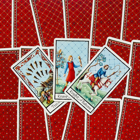 tarot kortos su raudonomis nugarėlėmis, trijų atverstų kortų fanuojantis išdėstymas ir klasikinis iliustracijų stilius