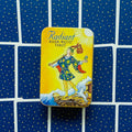 Tarot kortos Radiant Rider‑Waite metalinėje geltonoje dėžutėje, centre ant išskleistų mėlynų kortų nugarėlių su mažomis žvaigždėmis