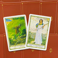 Tarot kortos, dvi atverstos kortos iš arti — Dešimt lazdelės ryškiai žaliame peizaže ir Devyni pentakliai su moterimi