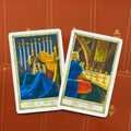 Tarot kortos, dvi atviros kortos (Nine of Swords ir Nine of Cups) su ryškiu raudonu fonu ir baltu rėmeliu, parodytos kampu