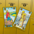 Tarot kortos Symbolon su aukso rėmeliais — dvi atverstos kortos (klajotojas ir ramentinis) ant geltono fono, demonstruoja skirtingus iliustracijų variantus