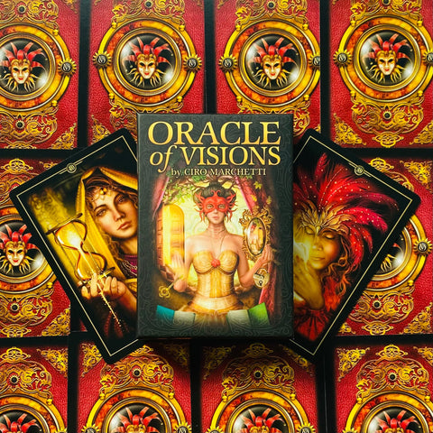Oracle of Visions kortų rinkinys Ciro Marchetti — dėžutė centre, dvi atverstos iliustruotos kortos ir ryškūs raudoni‑auksiniai nugarėlių raštai