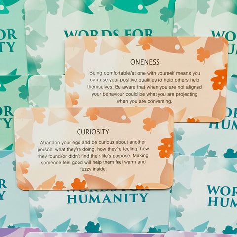 Inspiracinės kortelės Words for Humanity, artimas planas dviejų persikinių oranžinių kortelių „Oneness“ ir „Curiosity“ su tekstu
