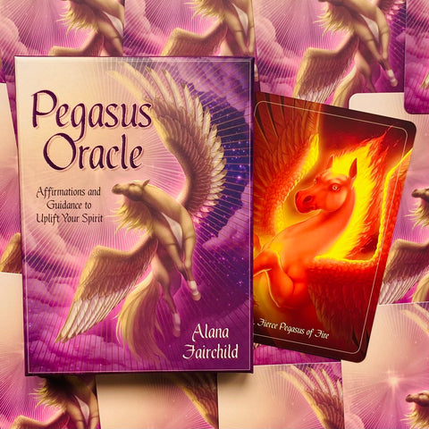 Pegasus oracle kortos violetinėje dėžutėje su auksinėmis sparnų iliustracijomis ir šalia ištrauktas ugninis kortos variantas