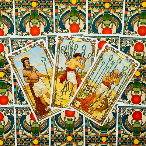 Tarot kortos su egiptietišku nugarėlių raštu, trys atverstos Lazdų kortos (9 ir 10) centre ant spalvoto fono