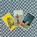 tarot kortos Rider‑Waite: trys Kalavijų kortos išdėstytos fanuote ant mėlyno raštuoto fono, matomas kortų priekis ir iliustracijos