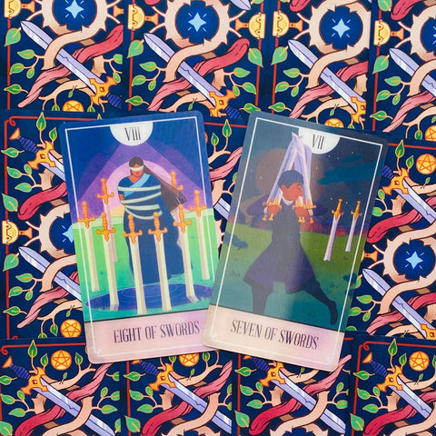 Tarot kortos — dvi atviros kortos (Eight of Swords ir Seven of Swords) matomos iš priekio ant ryškaus raštuoto mėlyno fono