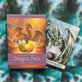 Dragon Path orakulo kortos, violetinė dėžutė su auksiniu drakonu ir šalia atversta sidabrinė korta, matomas dėžutės priekis ir kortos variantas