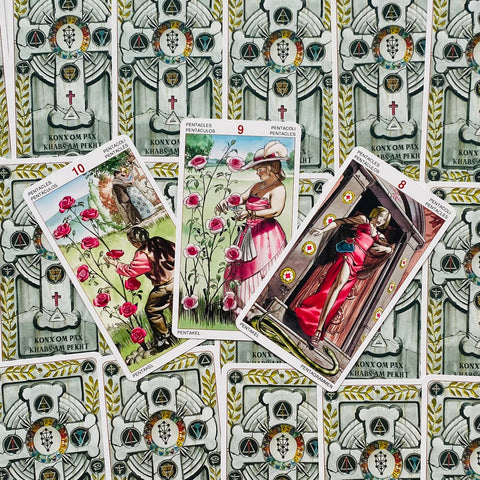 Tarot kortos — trijų Pentaklių kombinacija su rožėmis ir rožinėmis suknelėmis, fanuotos iš viršaus ant dekoratyvių nugarėlių