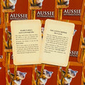Aussie Affirmations kortos, raudonas fonas ir dvi atverstos priekinės kortelės su įkvepiančiais tekstais „Hard Yakka“ ir „You Little Ripper“, puiki dovanų versija