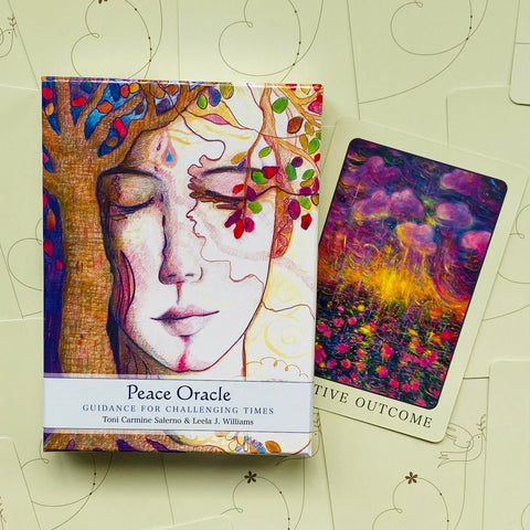 Peace Oracle kortos dėžutėje su spalvinga priekinė iliustracija ir atversta viena korta, rodanti meninį kortų dizainą