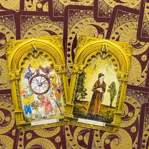 tarot kortos su auksiniais arkos rėmeliais, atviros Major Arcana — Likimo ratas ir Eremitas, bordo kortelių fone