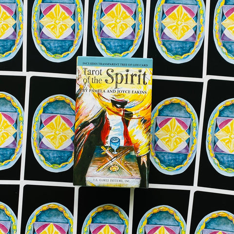 Tarot kortos Tarot of the Spirit dėžutė su spalvingu viršeliu, centrinė nuotrauka ant išskleistų kortų nugarėlių fono
