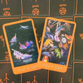 Tarot kortos su oranžiniu rėmeliu: „Eight of Cups“ ir „Seven of Cups“ padėtos ant juodo simbolinio fono, pasvirusios kampu
