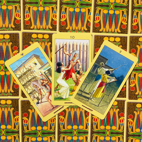 Tarot kortos Egipto tematikos rinkinys su geltonais kraštais, trys atverstos kortos fanuotos ant dekoratyvių nugarėlių, matomi detalūs piešiniai