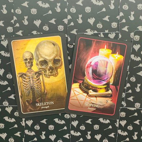 Tarot kortos su Skeleton ir Scrying variantais — geltonos skeletas ir rožinis kristalų rutulys ant juodo Helovino fono