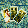 Tarot kortos trijų kortų priekinis išdėstymas (Pentaklių rinkinys: 9, 10 ir rūmų korta) ant mėlyno ornamentuoto fono, artimas planas