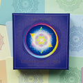 Kortų rinkinys Dimensions of Light violetinėje dėžutėje su spalvota mandala centre, padėtas ant pastelinio numeruoto fono
