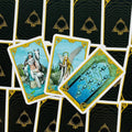 Tarot kortos su mėlynais ir auksiniais rėmais, trijų atverstų kortų fanuota kompozicija, pabrėžianti individualias iliustracijas