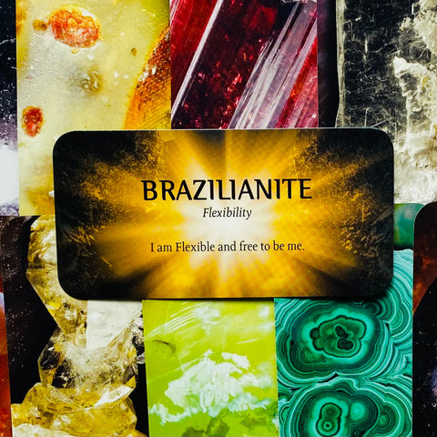 Brazilianite kortelė su auksiniu spindesiu ir užrašu „I am Flexible and free to be me“, pateikta ant spalvoto mineralų koliažo