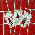 Tarot kortos su raudonomis nugarėlėmis, centre trys atverstos Puodelių figūros — jaunuolis, riteris ir karalienė