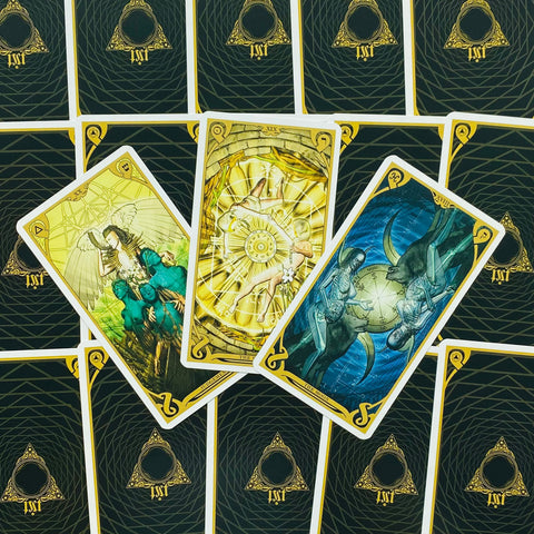 Tarot kortos su trijomis atvertomis kortomis (Saulė, Teismas, Mėnulis), geltoni ir mėlyni piešiniai ant juodo‑auksinio nugarėlio, unikalus variantas galerijoje